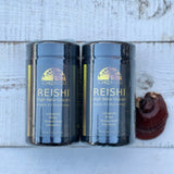 Two Schizarefu Reishi containers on a wooden surface with a mushroom in the background.