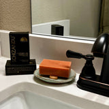 Orange bar of soap on a soap dish next to a black box labeled 'Schizzandu' on a bathroom sink.