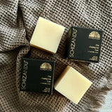 Three shampoo bars with packaging, placed on a textured surface.