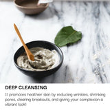 Black bowl with skincare product on a marble surface, text about deep cleansing benefits.
