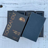 A black bar of soap named 'THE charcoal detox bar' by SCHIZANDU, displayed on a wooden surface with the packaging behind it.