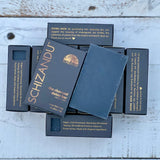A black bar of soap named 'THE charcoal detox bar' by SCHIZANDU, displayed on a wooden surface with the packaging behind it.