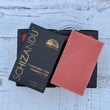 A French pink clay cleansing bar next to its black packaging, labeled SCHIZANDU, on a wooden surface.