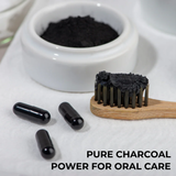Black charcoal powder in a bowl with a toothbrush and capsules on a white surface, labeled 'Pure Charcoal Power for Oral Care'.