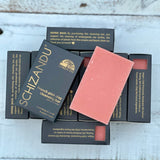 A French pink clay cleansing bar next to its black packaging, labeled SCHIZANDU, on a wooden surface.