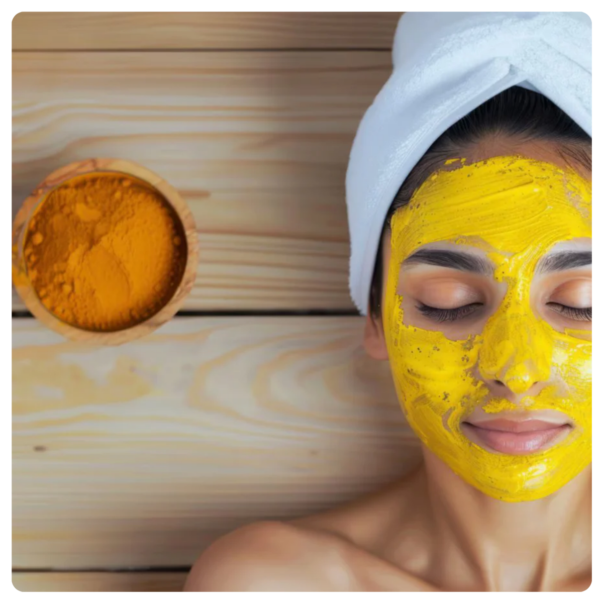 A woman with a white towel wrapped around her hair rests against a light wood background, wearing a bright yellow face mask. A small wooden bowl filled with orange-yellow powder sits to the left.