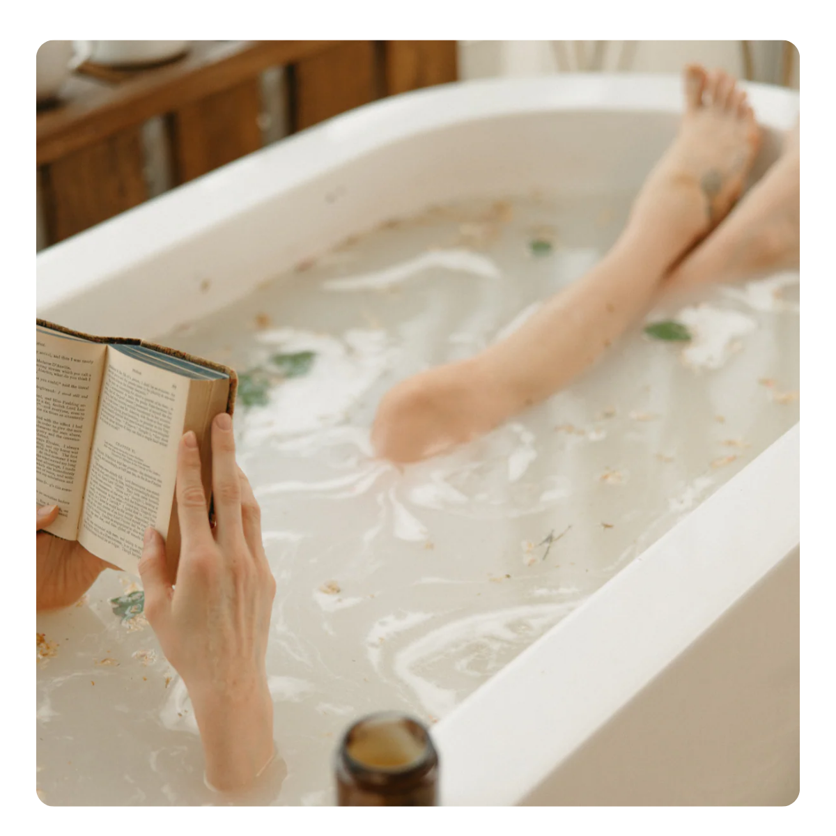 Person reading a book in a bathtub filled with bubbles and flowers.