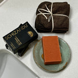 Bar of soap on a plate with Schizandu packaging and folded towels on a white surface