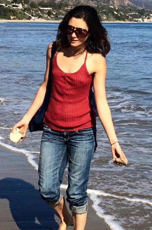 Woman in red tank top and blue jeans walking on a beach.