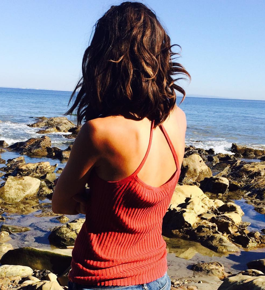 Person wearing a red tank top standing on a rocky beach with ocean view