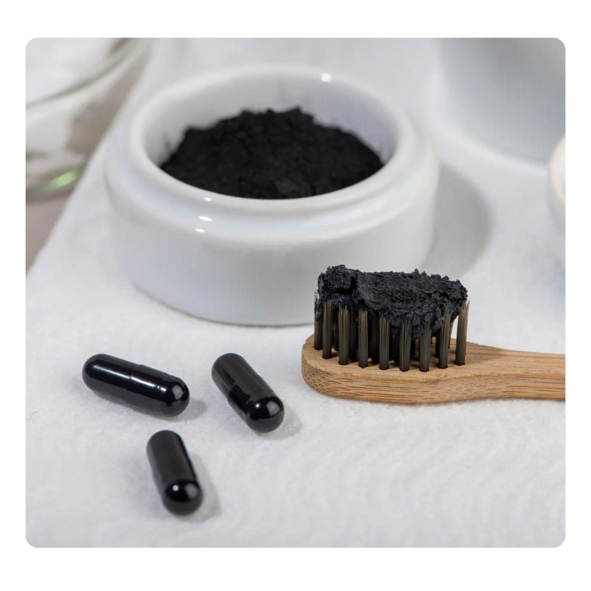 Black toothpaste, capsules, and a toothbrush with black powder on a white background
