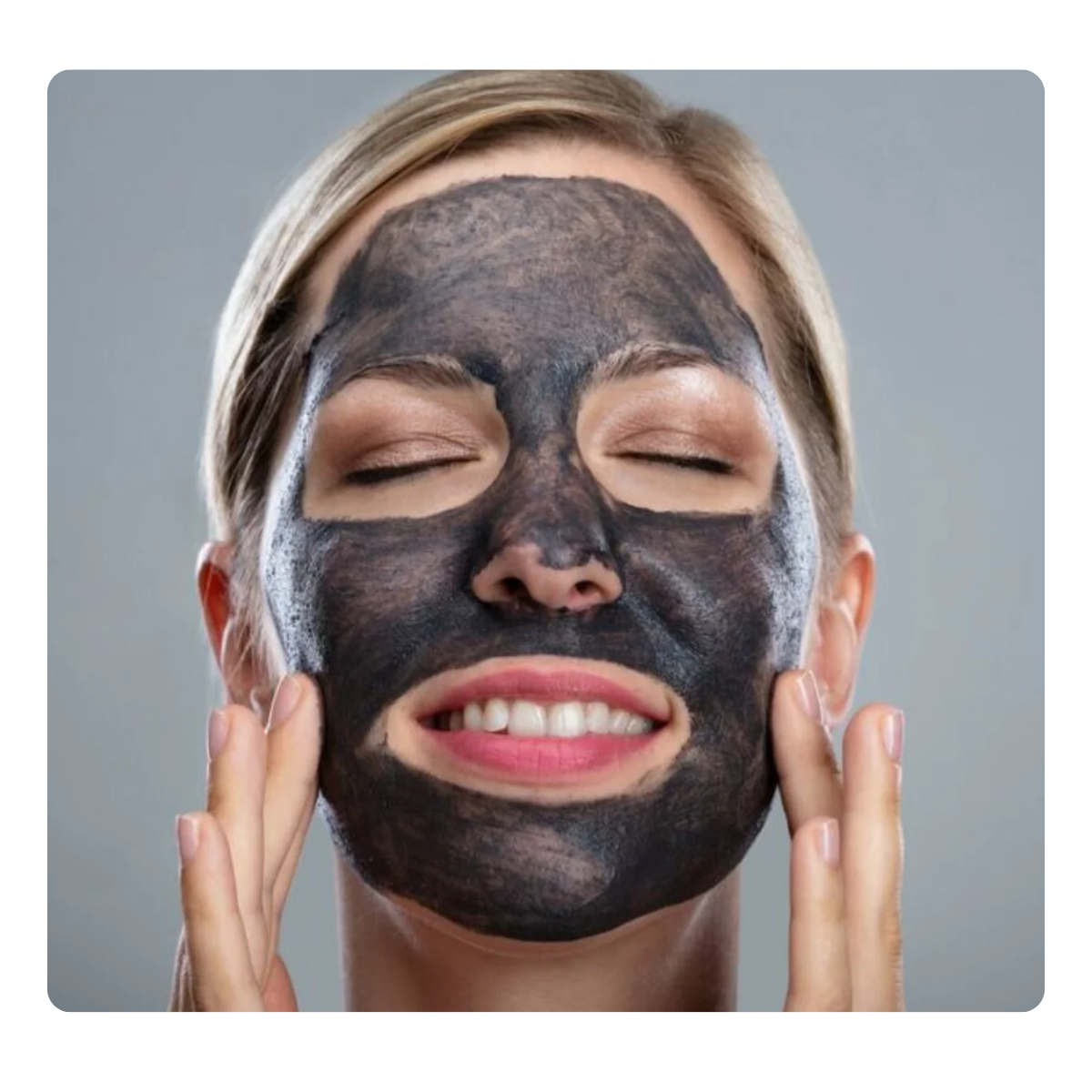 Woman applying a black facial mask against a gray background