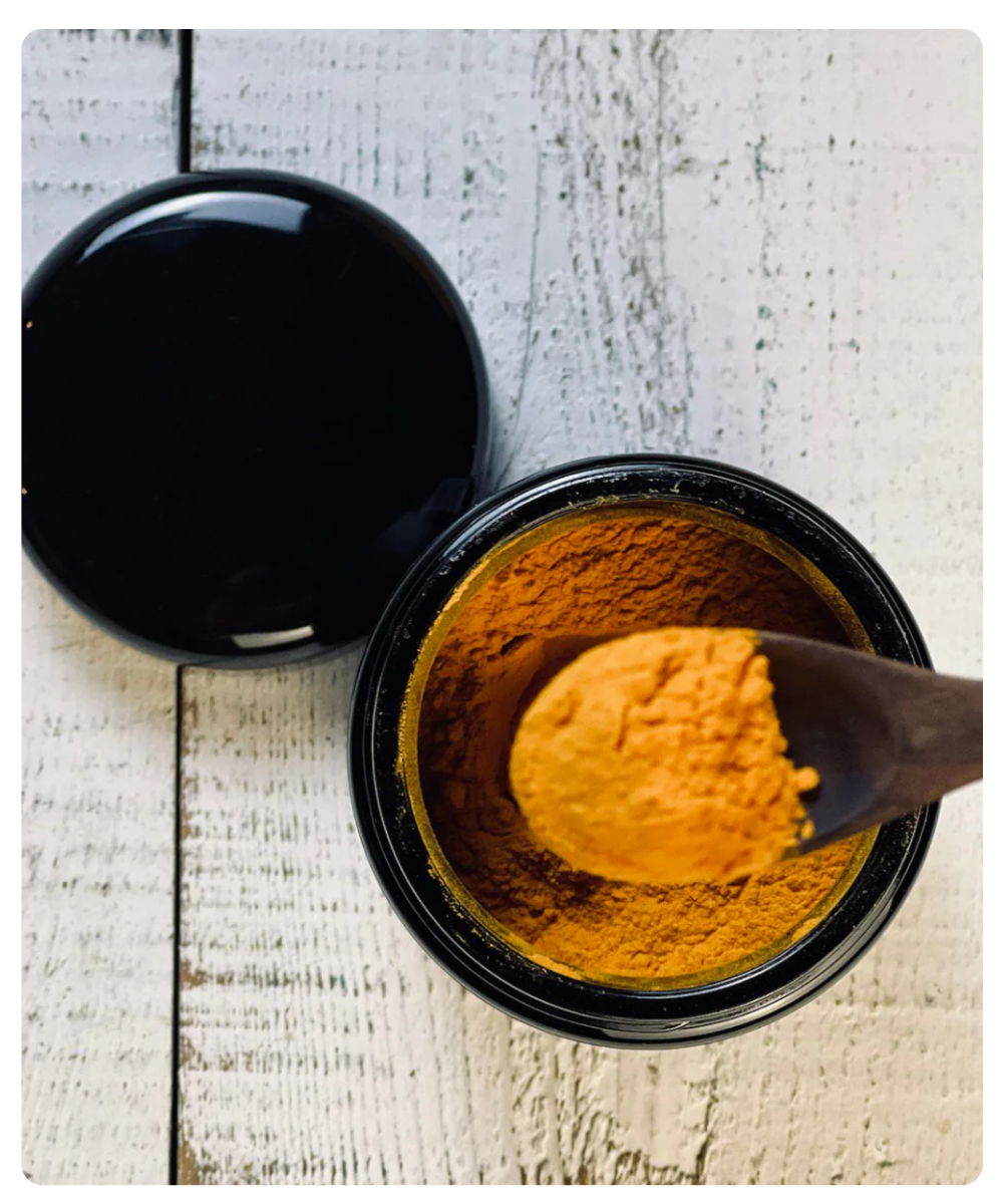 Open container of turmeric powder with a wooden spoon on a wooden surface