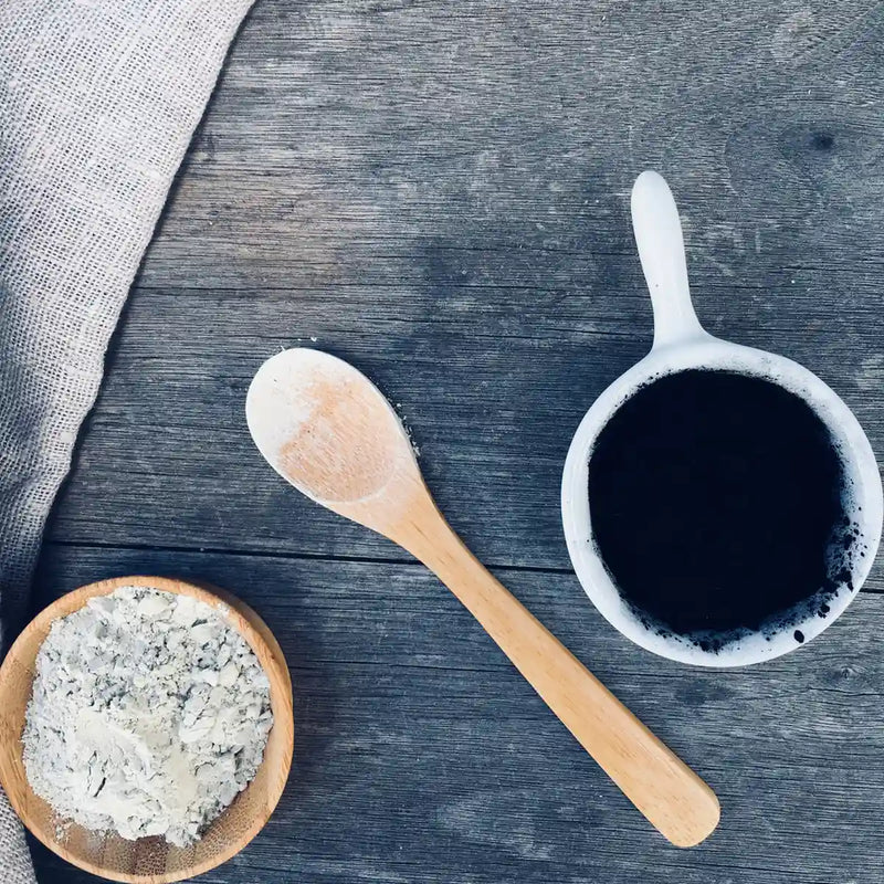 Bentonite Clay and charcoal powder in different cups with a wooden spoon in between, Schizandu