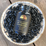 Schizkin Organic Coconut Activated Charcoal supplement bottle surrounded by capsules on a wooden surface
