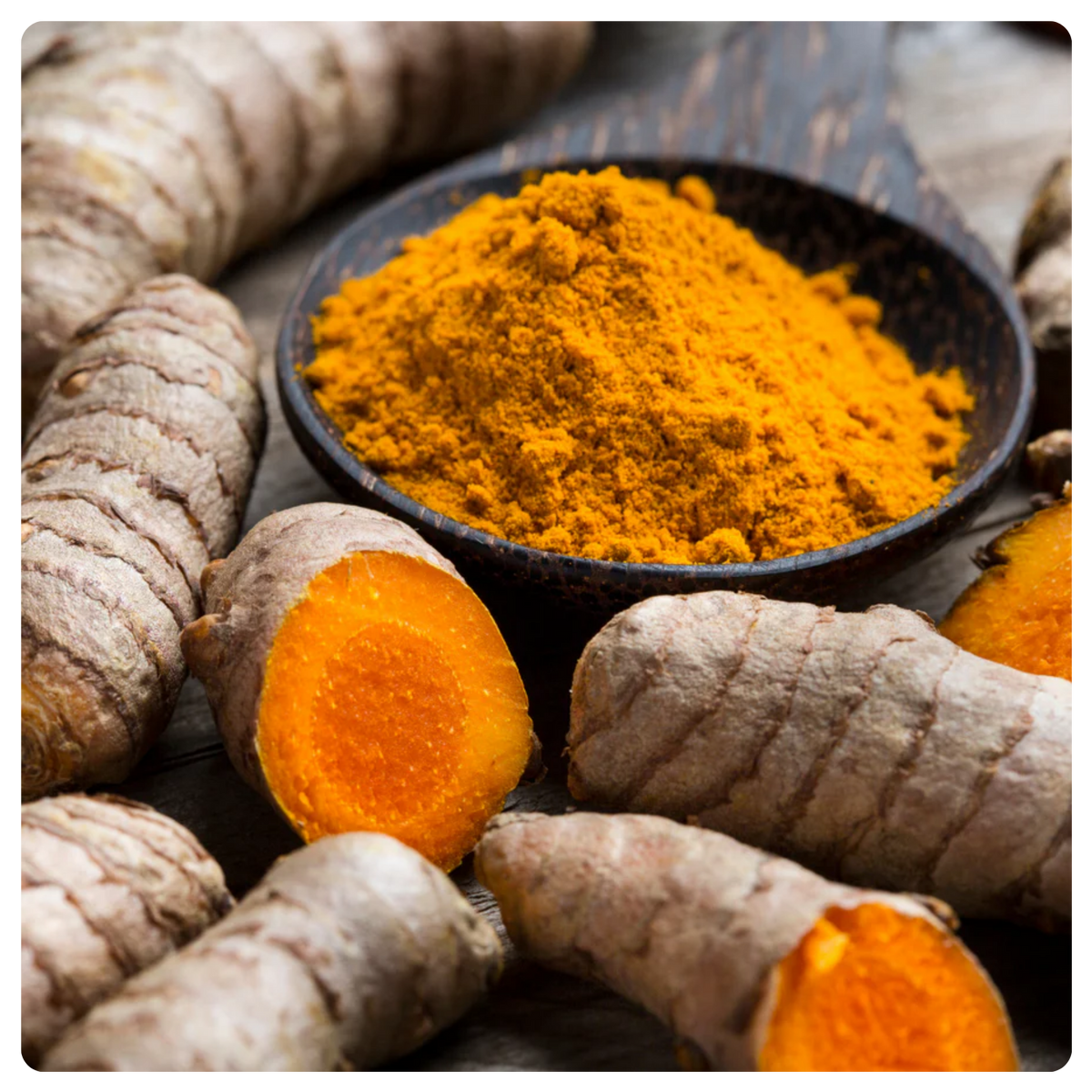 Turmeric root pieces and a small dark bowl filled with bright yellow-orange turmeric powder on a rustic wooden surface.