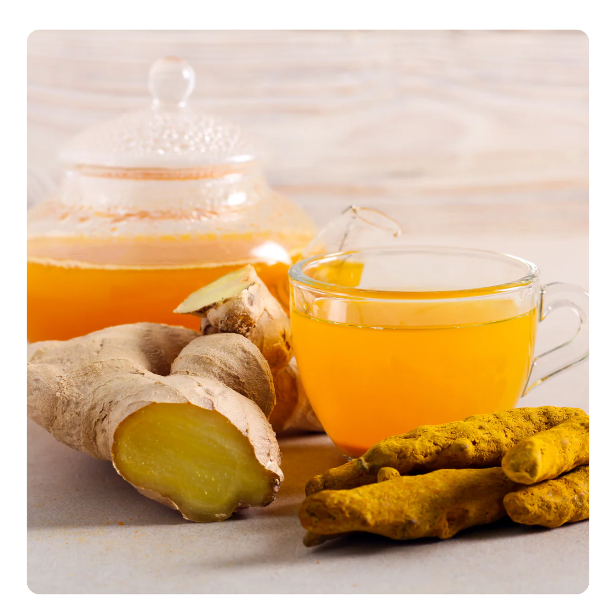 Glass of ginger tea with a teapot, ginger root, and turmeric on a light background