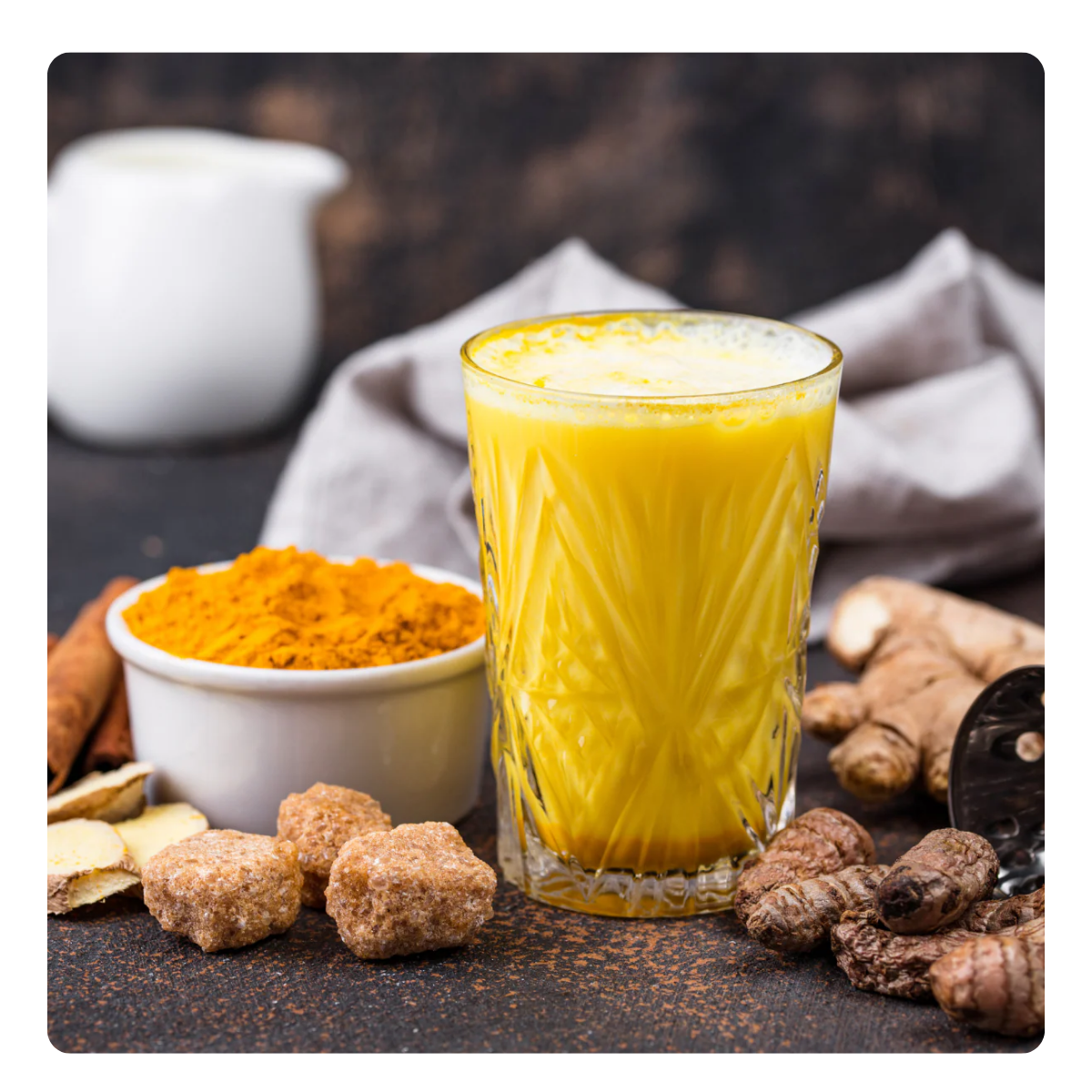 Glass of yellow juice with turmeric, sugar, and a teapot on a dark surface