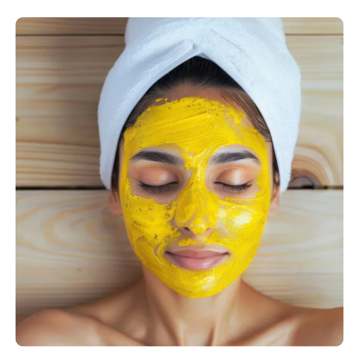 Woman with a curcumin yellow facial mask on her face, wrapped in a white towel.