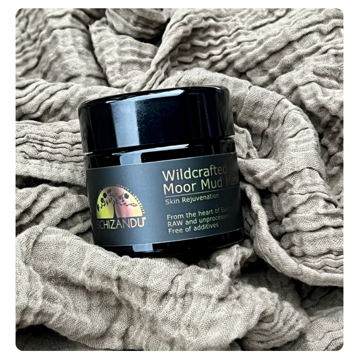 A black jar of schizandu Wildcrafted Moor Mud Mask resting on a textured, crinkled beige fabric background.