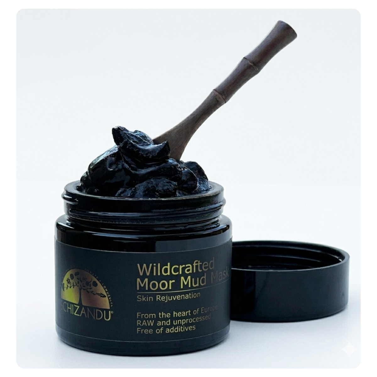 An open black jar of schizandu Wildcrafted Moor Mud Mask with a bamboo-style applicator spoon resting inside, shown against a clean white background with the lid placed beside the jar.