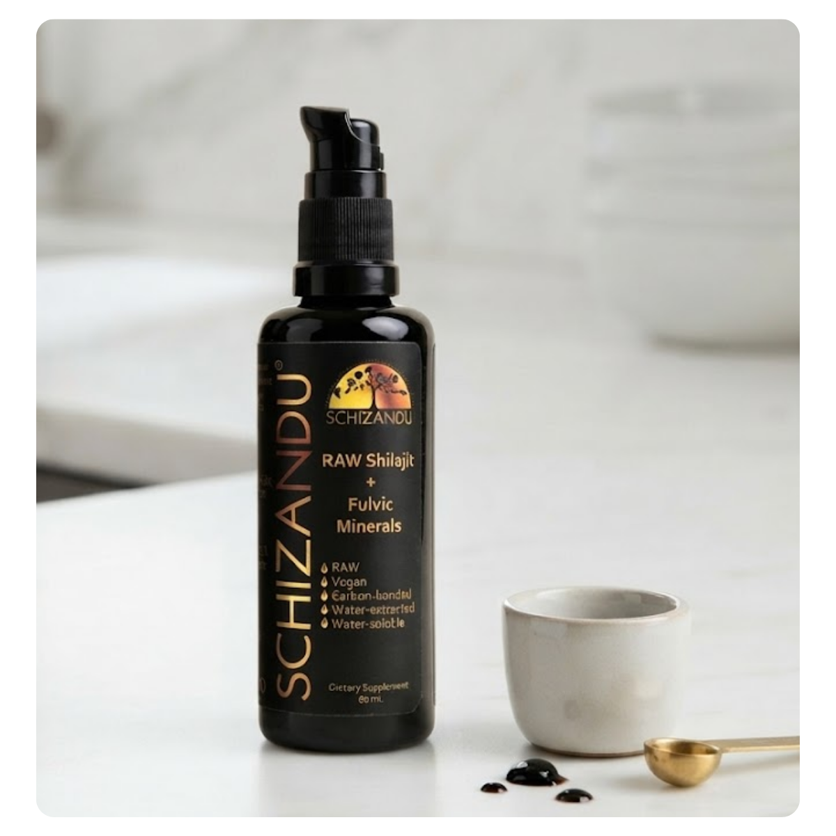 A bottle of Schizandu Raw Shilajit + Fulvic Minerals dietary supplement, shown on a light marble surface next to a small white cup, a gold spoon, and a few dark clumps of the product.