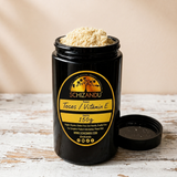A Miron glass jar of Schizandu Tocos / Vitamin E supplement with the product showing at the top, shown on a rustic white wooden surface with the lid placed beside it. The background is a soft beige studio-style backdrop.